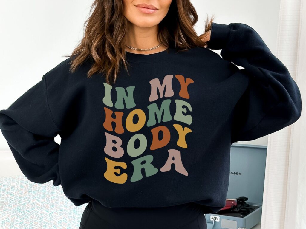 Woman wearing an oversized sweatshirt that says In My Homebody Era.