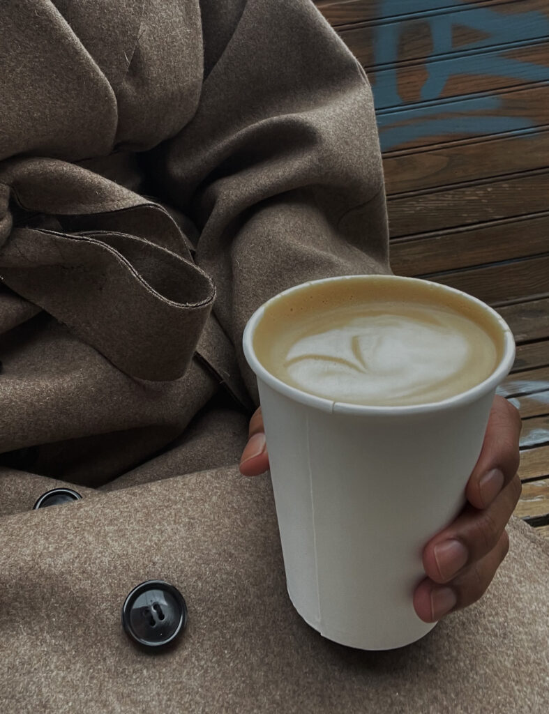Woman in a cozy-looking wool coat holding a hot latte.